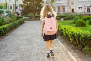 A child wearing a school uniform and a rucksack walks on a path alone.